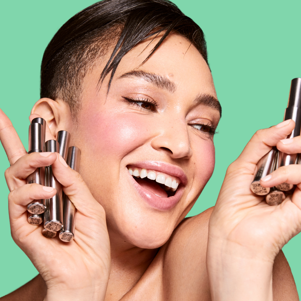 Woman holding makeup products against a green background